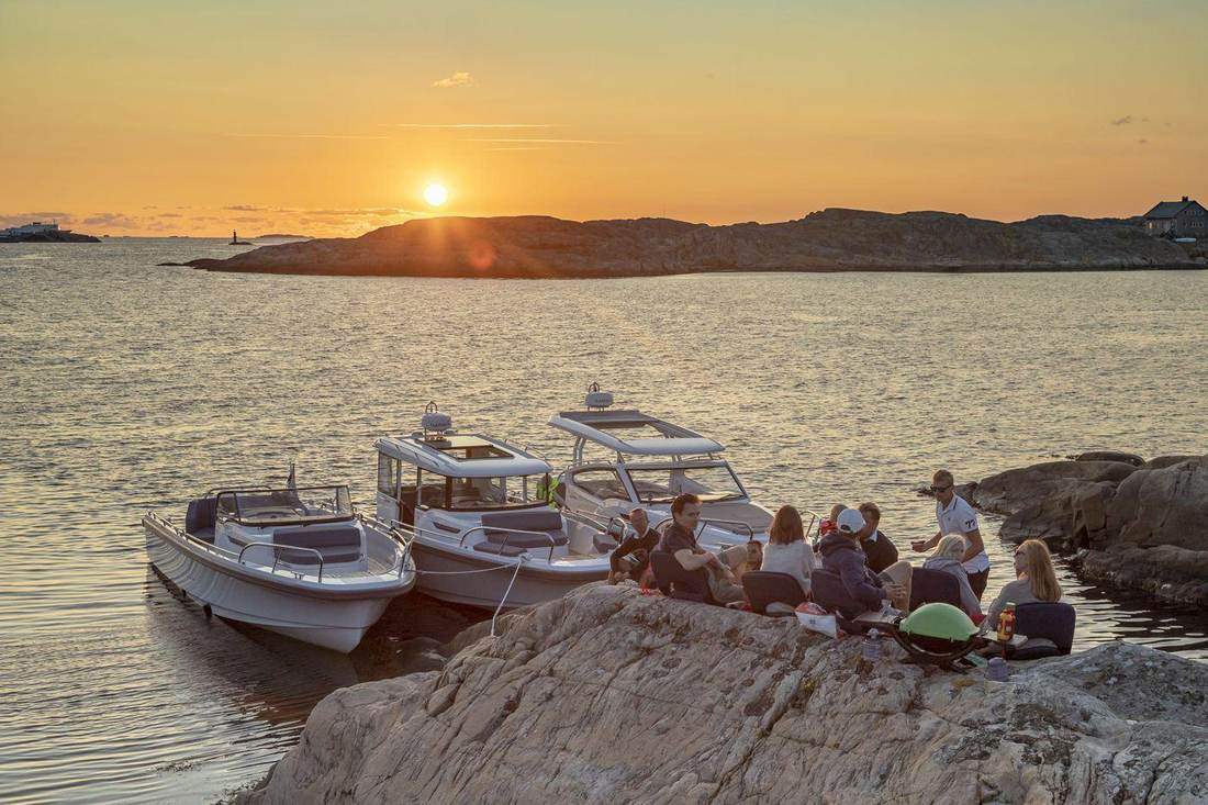 Venner samlet rundt et bål ved to båter i solnedgang